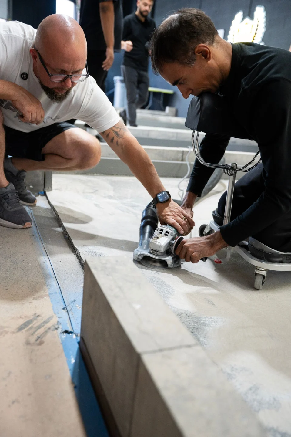An instructor guides a student using an edge grinder with a dust shroud along a practice floor