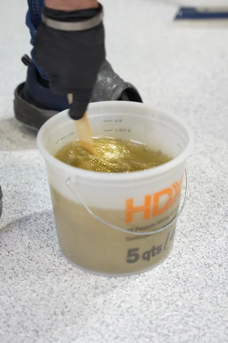 Gold glitter is stirred into clear epoxy in a bucket on a finished flake floor
