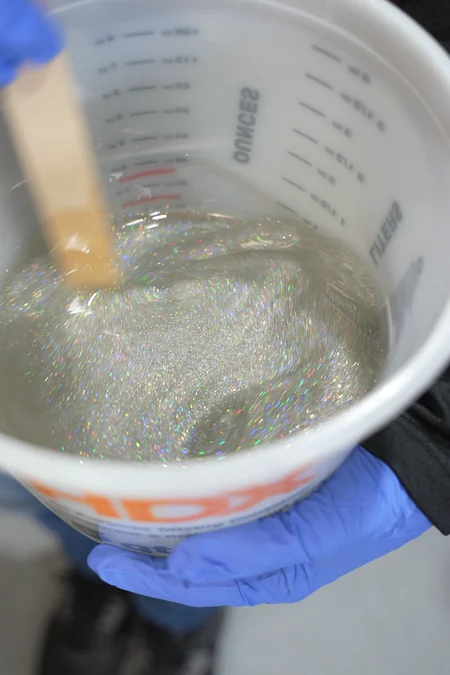 Holographic glitter is stirred into clear epoxy in a mixing bucket