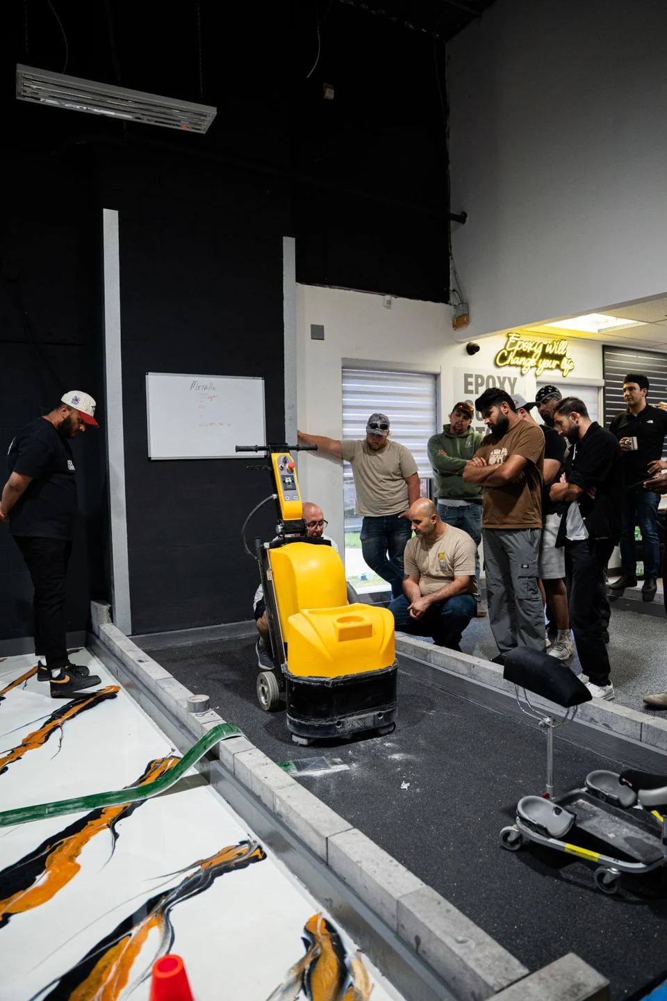 An instructor demonstrates a planetary floor grinder on a practice bay while students watch