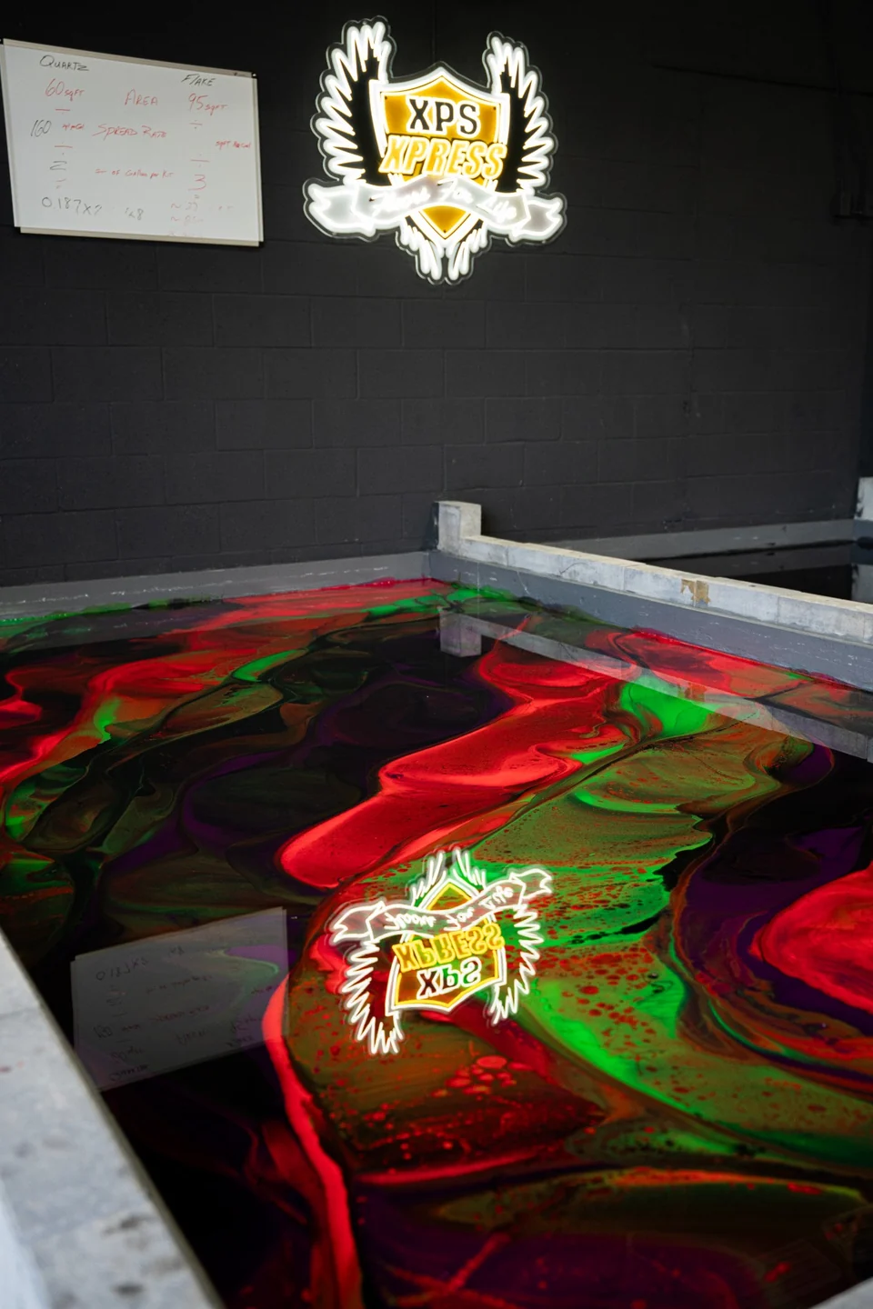 A red and green metallic epoxy practice floor reflecting the illuminated XPS Xpress sign