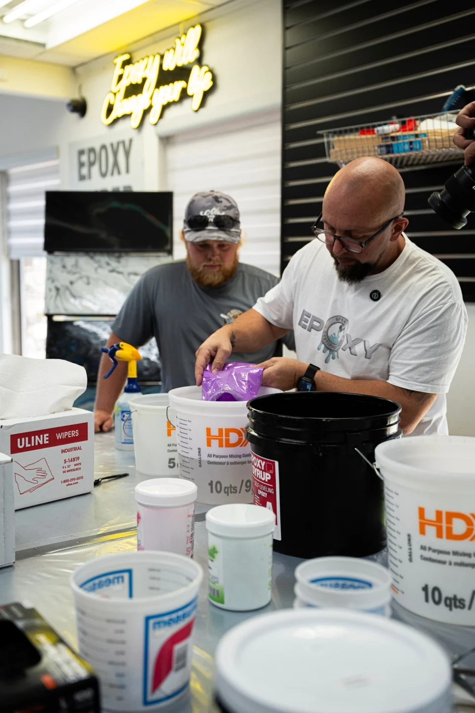 An instructor adds pigment to a bucket of epoxy while a student watches