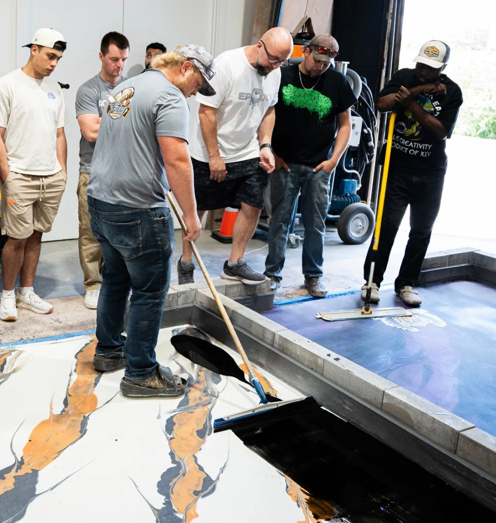 A student draws black epoxy across a white and orange metallic floor with a squeegee